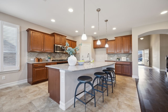 kitchen featuring pendant lighting, stainless steel appliances, a kitchen breakfast bar, light stone counters, and a center island with sink