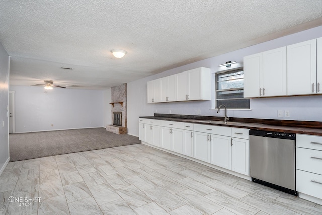 kitchen featuring ceiling fan, white cabinets, a textured ceiling, a stone fireplace, and stainless steel dishwasher