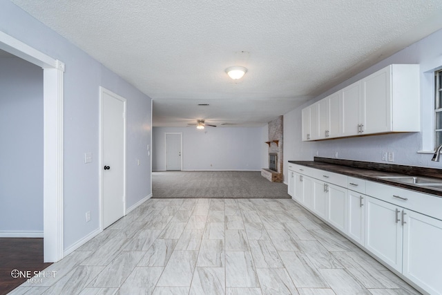 kitchen with sink, a textured ceiling, ceiling fan, a fireplace, and white cabinets