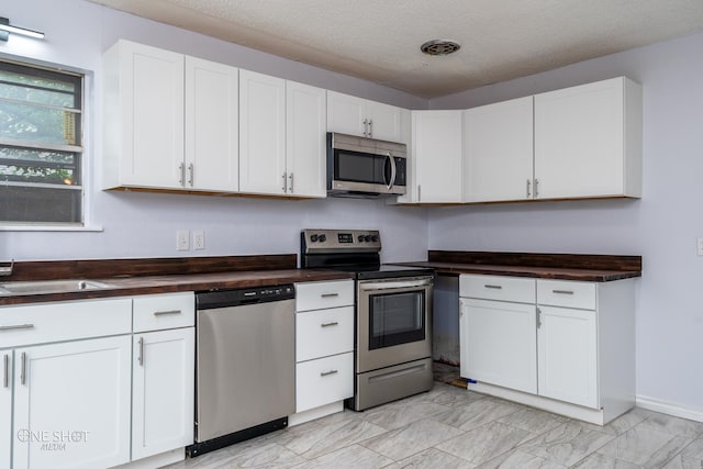 kitchen featuring white cabinetry, appliances with stainless steel finishes, butcher block counters, and a textured ceiling