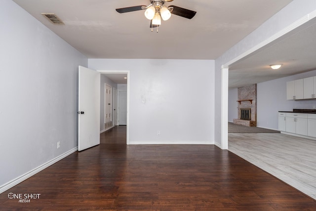 empty room featuring dark hardwood / wood-style flooring, a large fireplace, and ceiling fan