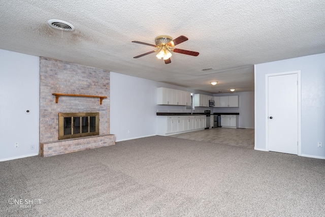 unfurnished living room with sink, ceiling fan, carpet, a textured ceiling, and a brick fireplace