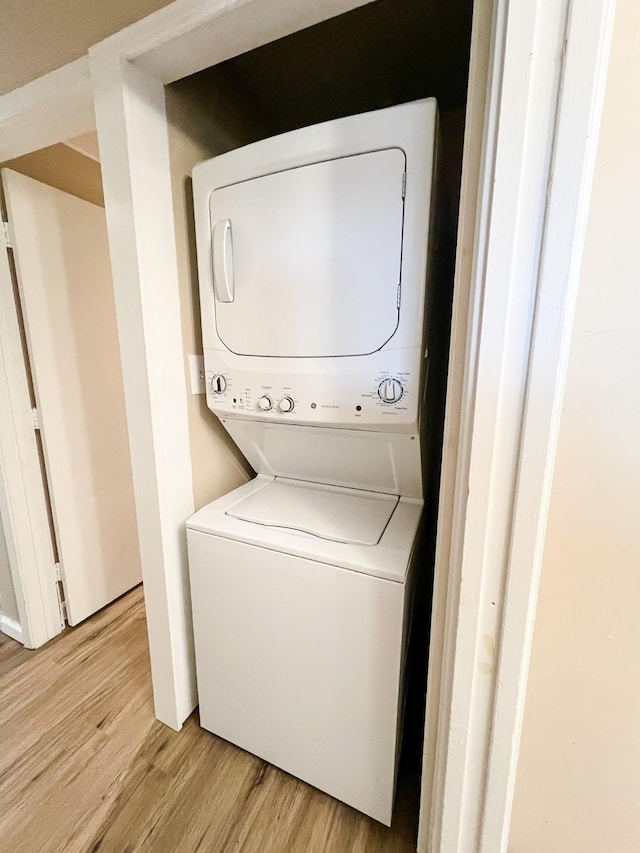 clothes washing area featuring stacked washer and clothes dryer and light hardwood / wood-style flooring