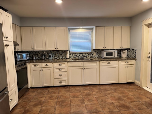 kitchen with tasteful backsplash, white cabinetry, sink, stainless steel fridge, and dark tile patterned floors