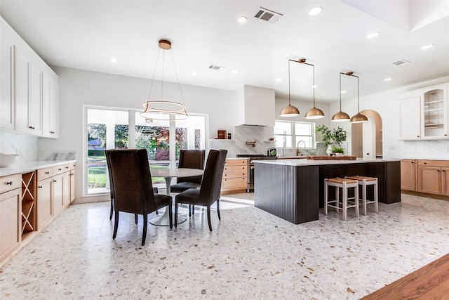 kitchen featuring stainless steel stove, white cabinets, a kitchen island, decorative backsplash, and wall chimney exhaust hood