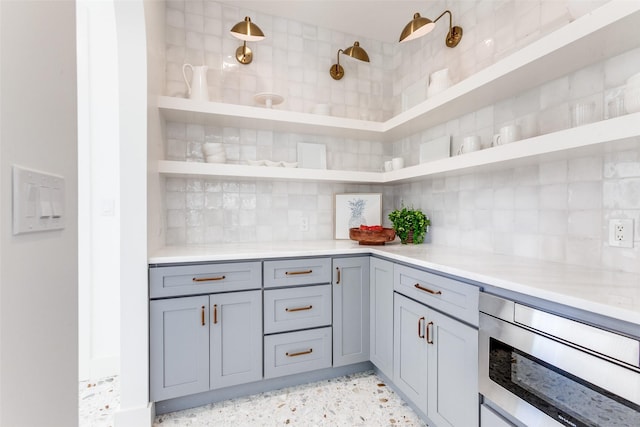 kitchen with hanging light fixtures, gray cabinetry, stainless steel microwave, and decorative backsplash