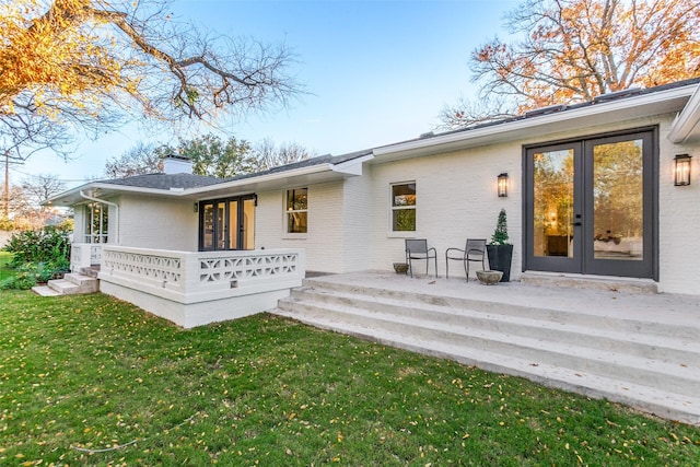 rear view of property featuring french doors, a patio area, and a lawn