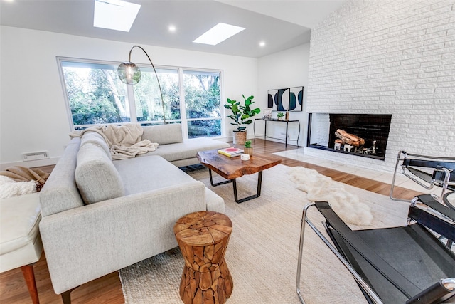 living room featuring a healthy amount of sunlight, vaulted ceiling with skylight, a brick fireplace, and light hardwood / wood-style flooring