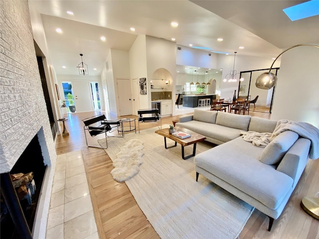 living room with an inviting chandelier, a fireplace, high vaulted ceiling, and light hardwood / wood-style flooring