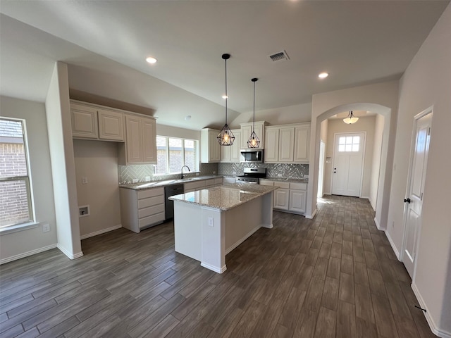 kitchen featuring appliances with stainless steel finishes, decorative light fixtures, sink, a center island, and light stone countertops