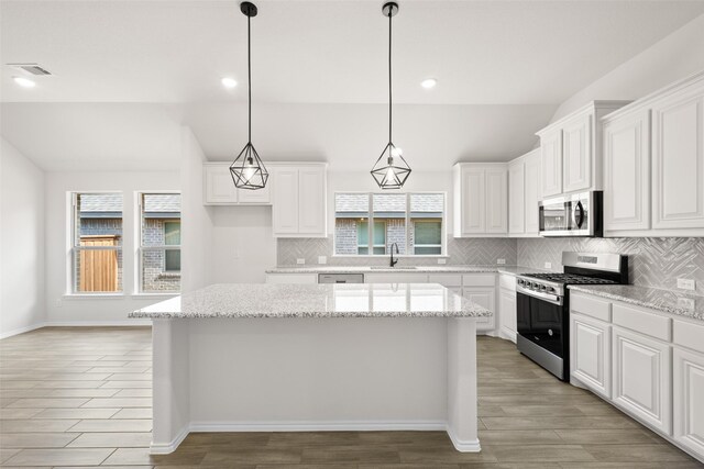 kitchen featuring sink, a center island, appliances with stainless steel finishes, pendant lighting, and light stone countertops