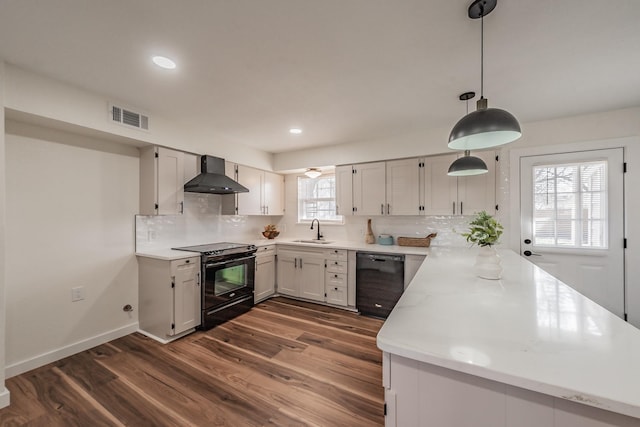 kitchen featuring sink, black appliances, hanging light fixtures, wall chimney range hood, and white cabinets