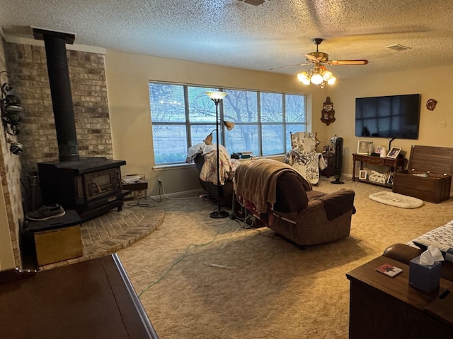 living room featuring ceiling fan, carpet, a wood stove, and a textured ceiling