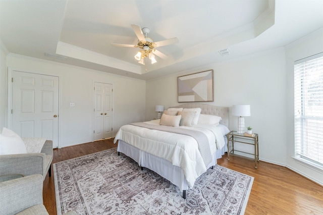 bedroom with a raised ceiling, multiple windows, and visible vents