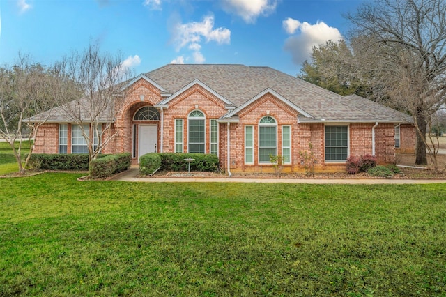 view of front facade featuring a front yard, brick siding, and roof with shingles