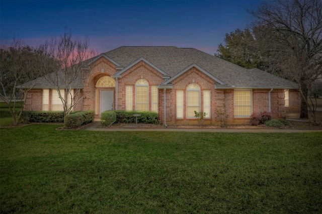 ranch-style house featuring a shingled roof, a front lawn, and brick siding