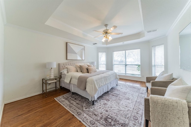 bedroom featuring a tray ceiling, visible vents, crown molding, and wood finished floors