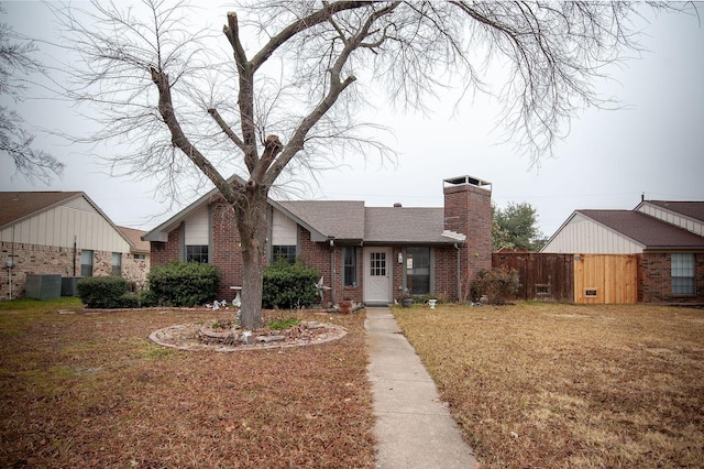 view of front of home with central AC, fence, a front yard, brick siding, and a chimney