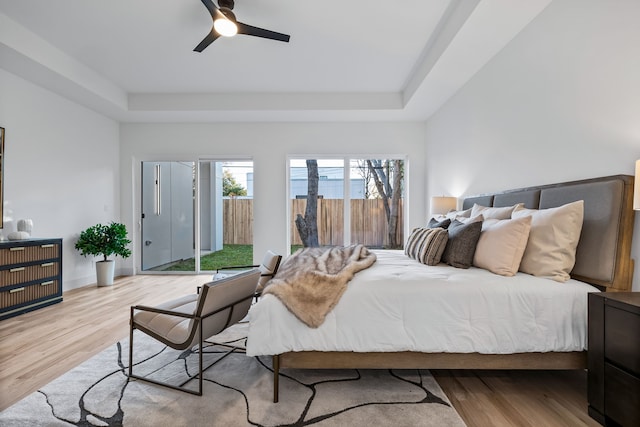 bedroom featuring a raised ceiling, access to exterior, ceiling fan, and light hardwood / wood-style flooring