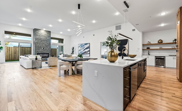 kitchen featuring wine cooler, a stone fireplace, sink, an island with sink, and light stone countertops