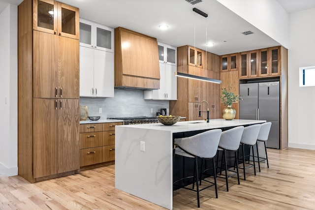 kitchen with an island with sink, appliances with stainless steel finishes, white cabinets, and light wood-type flooring