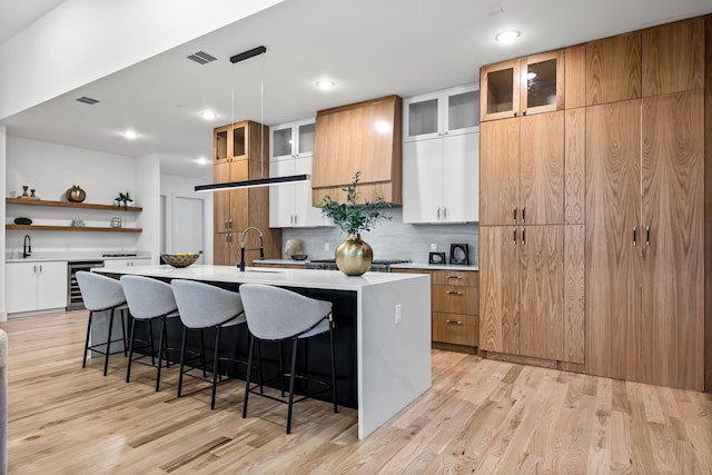 kitchen with white cabinetry, beverage cooler, hanging light fixtures, a kitchen island with sink, and light hardwood / wood-style flooring