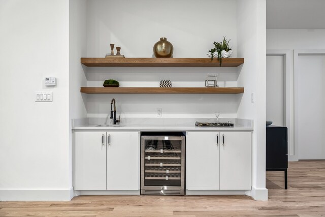 bar with white cabinetry, beverage cooler, sink, and light wood-type flooring