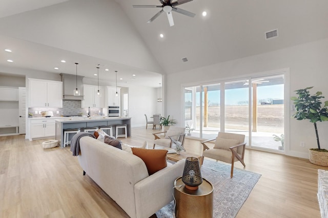 living room with ceiling fan, sink, high vaulted ceiling, and light hardwood / wood-style flooring