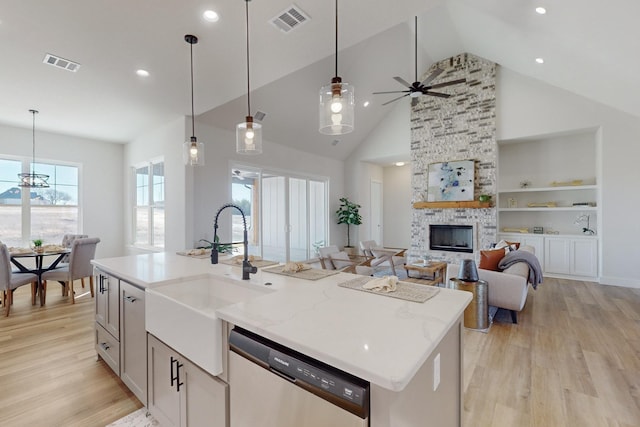 kitchen with built in features, decorative light fixtures, sink, stainless steel dishwasher, and a center island with sink