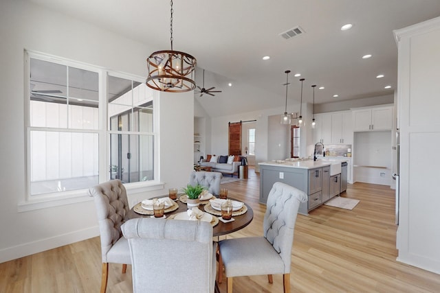 dining room with lofted ceiling, a barn door, ceiling fan with notable chandelier, and light wood-type flooring