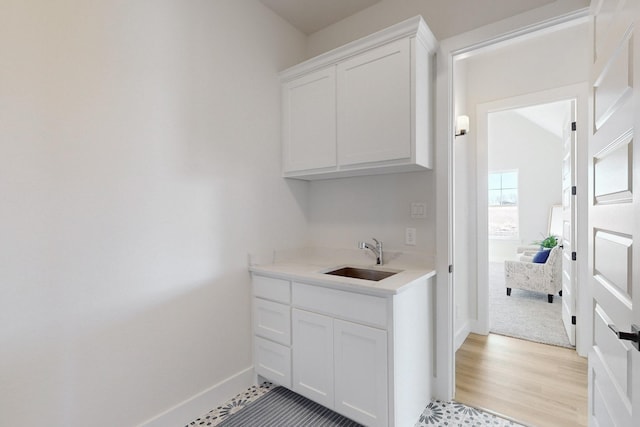 bar featuring light wood-type flooring, sink, and white cabinets