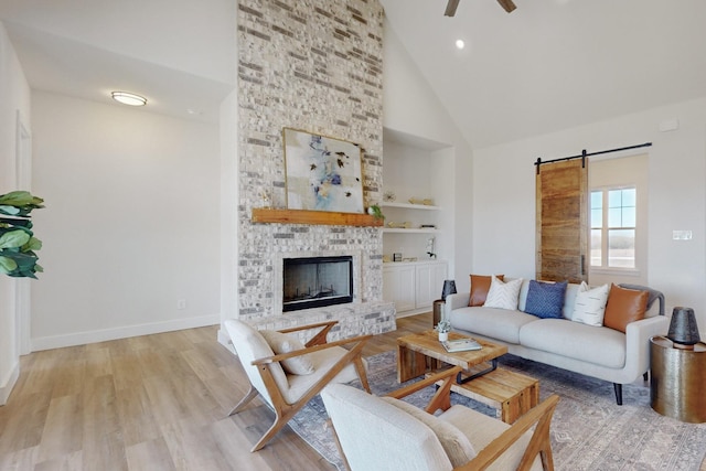 living room with a fireplace, high vaulted ceiling, light wood-type flooring, ceiling fan, and a barn door