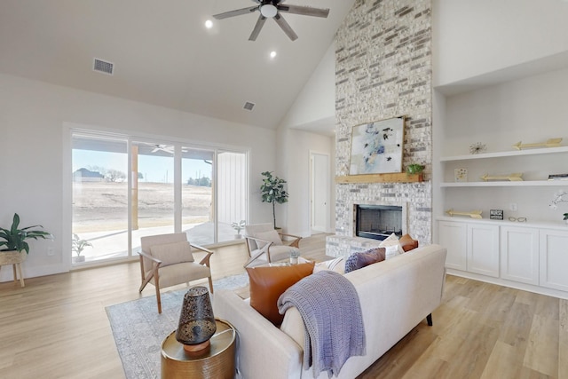 living room with a stone fireplace, high vaulted ceiling, light hardwood / wood-style flooring, built in features, and ceiling fan