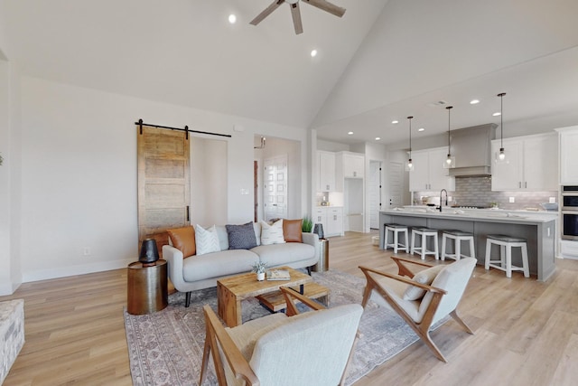 living room with sink, high vaulted ceiling, light hardwood / wood-style flooring, ceiling fan, and a barn door