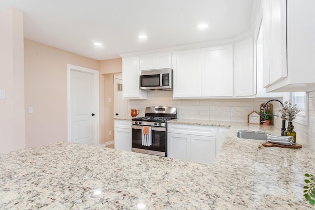 kitchen featuring sink, appliances with stainless steel finishes, tasteful backsplash, light stone counters, and white cabinets