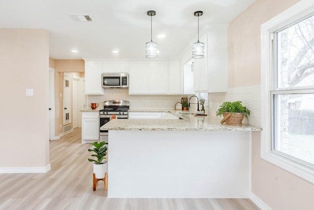 kitchen with appliances with stainless steel finishes, white cabinetry, sink, light stone counters, and kitchen peninsula