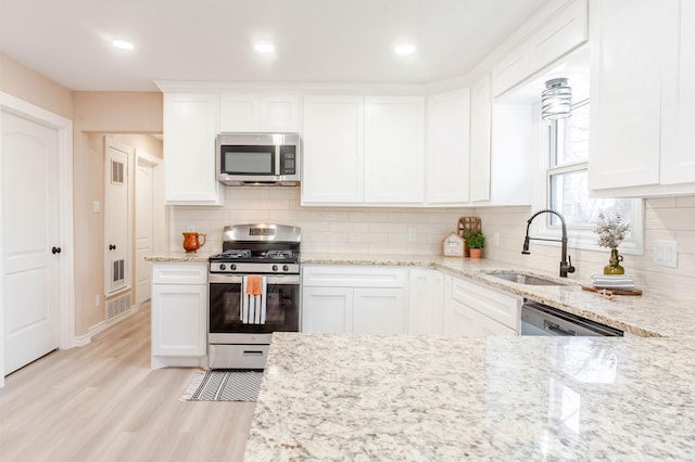 kitchen with sink, light stone counters, light wood-type flooring, appliances with stainless steel finishes, and white cabinets