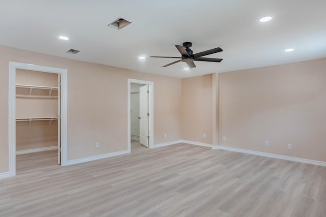 unfurnished bedroom with a walk in closet, ceiling fan, and light wood-type flooring