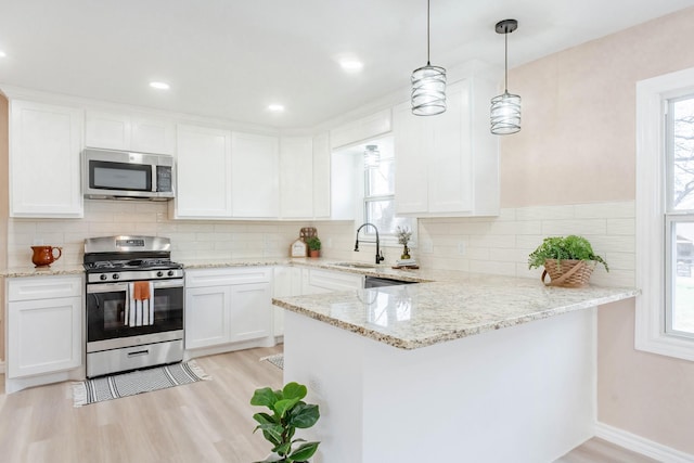 kitchen with sink, white cabinetry, hanging light fixtures, stainless steel appliances, and light wood-type flooring