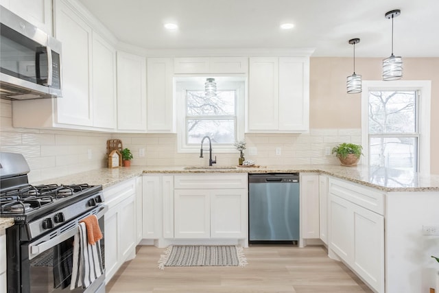 kitchen featuring sink, white cabinetry, appliances with stainless steel finishes, pendant lighting, and light stone countertops