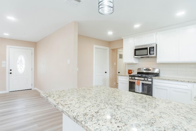 kitchen featuring appliances with stainless steel finishes, white cabinetry, decorative backsplash, light stone counters, and light wood-type flooring