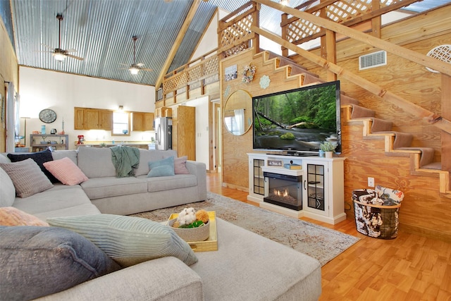 living room with high vaulted ceiling, light hardwood / wood-style floors, ceiling fan, and wood walls