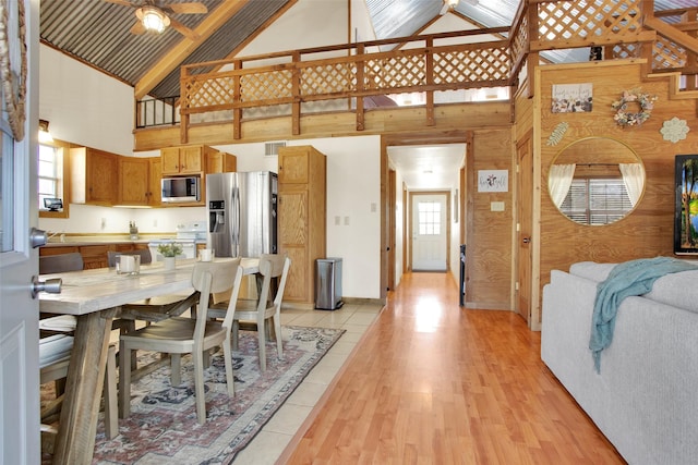 interior space with wood walls, high vaulted ceiling, light hardwood / wood-style flooring, ceiling fan, and stainless steel appliances