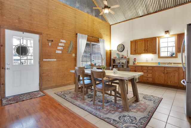 tiled dining space with ceiling fan, sink, wooden walls, and high vaulted ceiling