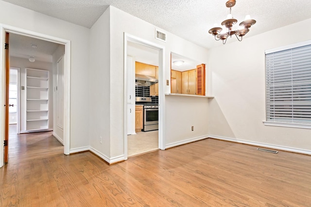 interior space with a chandelier, a textured ceiling, light wood-type flooring, and built in shelves