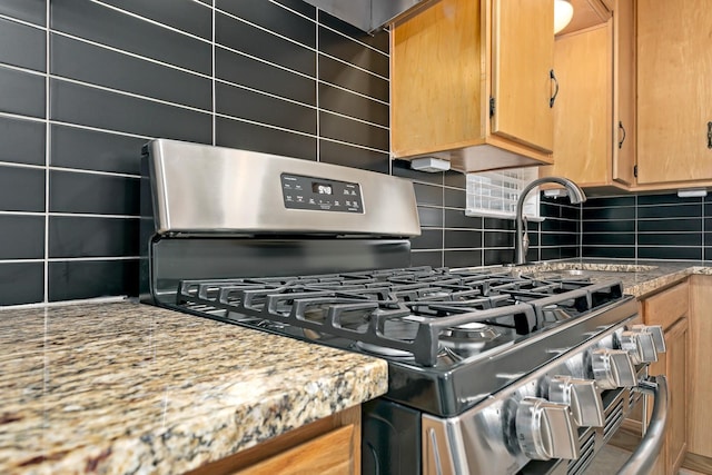 interior details with tasteful backsplash, stainless steel gas range oven, and light stone countertops