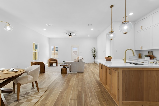 kitchen with sink, white cabinetry, a kitchen island with sink, light hardwood / wood-style floors, and decorative light fixtures