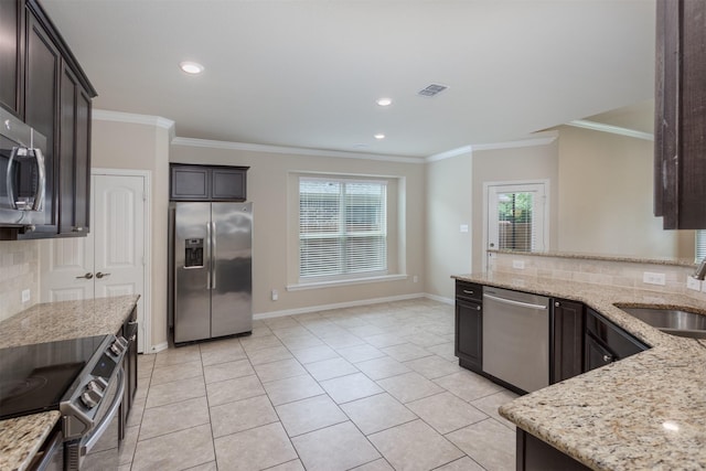 kitchen with crown molding, appliances with stainless steel finishes, light stone countertops, and dark brown cabinets