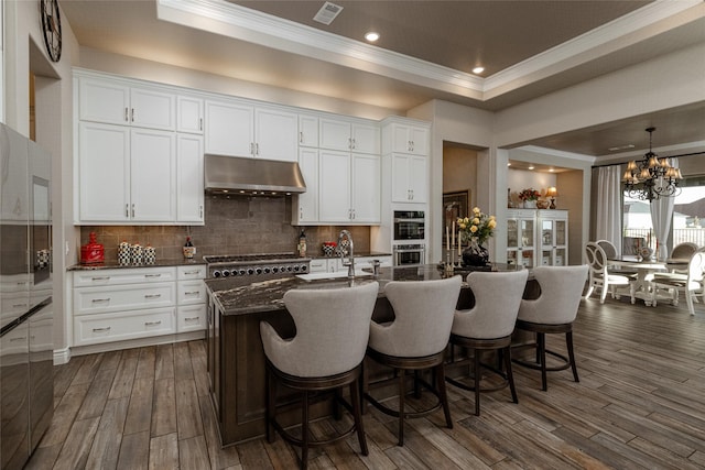 kitchen featuring a kitchen island with sink, stainless steel appliances, dark hardwood / wood-style floors, tasteful backsplash, and white cabinets