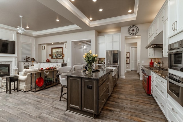 kitchen featuring crown molding, a breakfast bar area, a kitchen island with sink, white cabinetry, and a raised ceiling